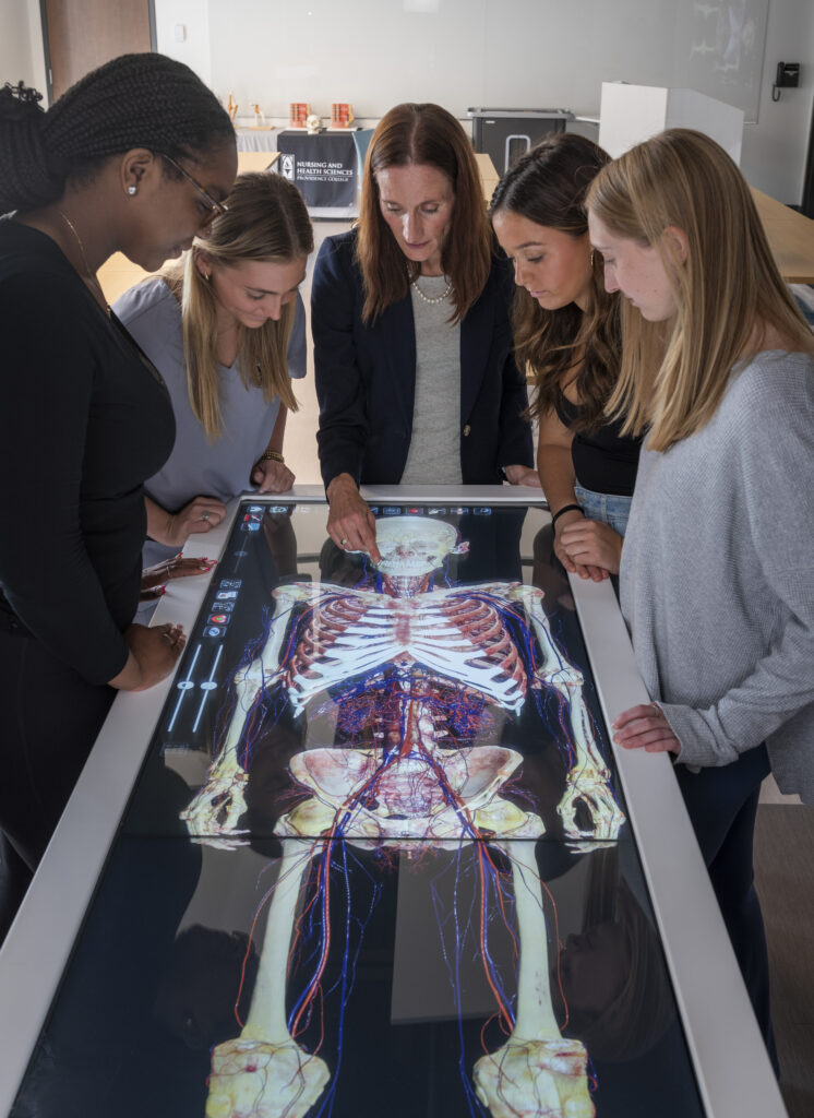 faculty and students look at Anatomage table with skeleton image. 